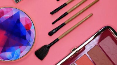 Stylish flatlay of makeup palettes and brushes on a pink background